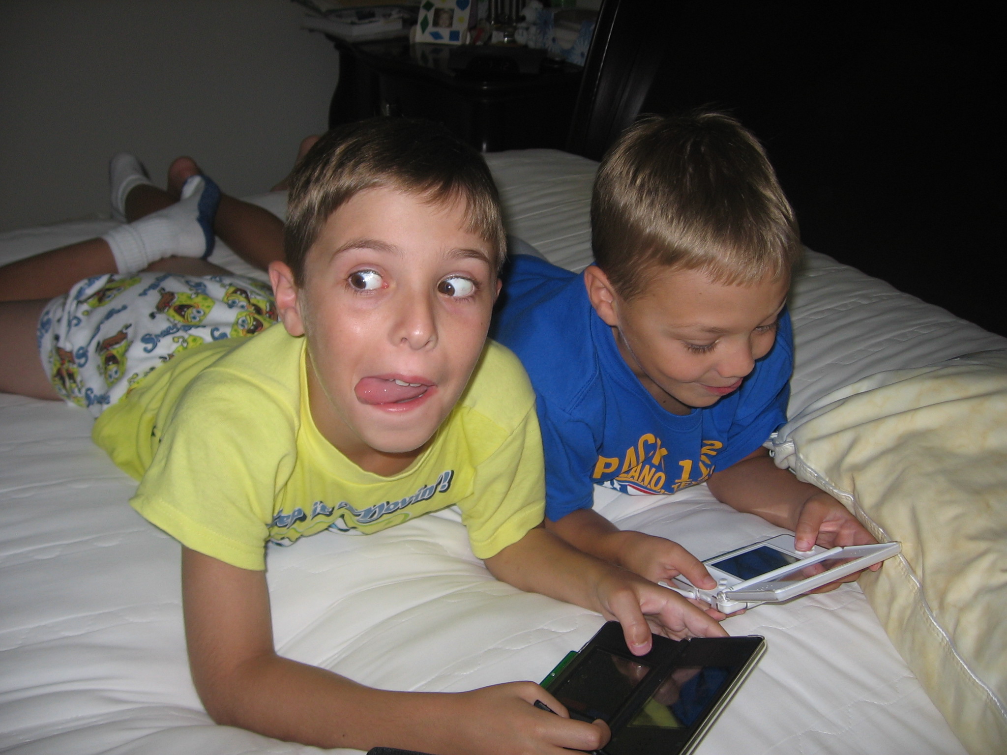 Two boys playing handheld games on a bed; Noah is on the right in blue.